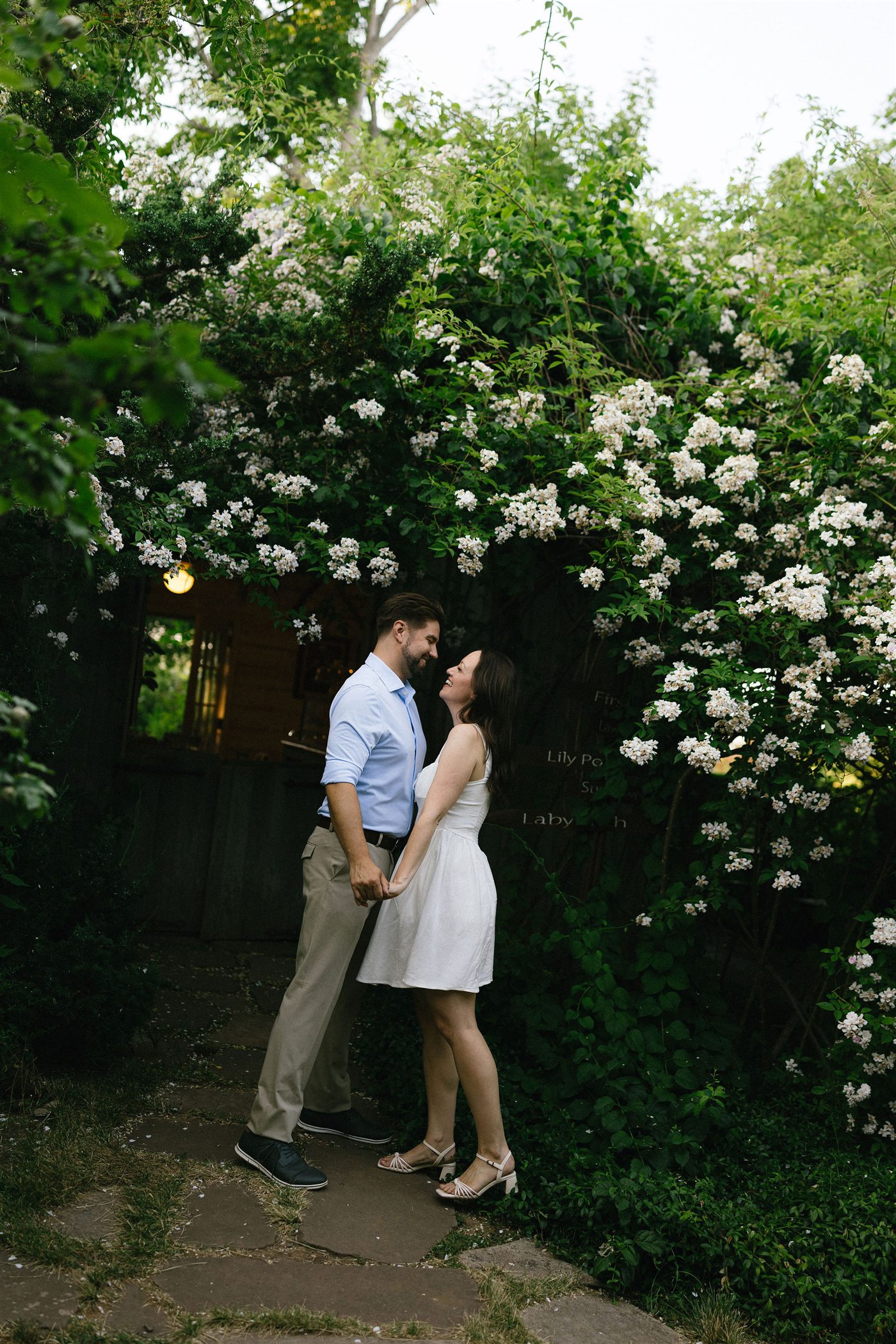 Danielle and Brenden laughing together beneath flowering vines