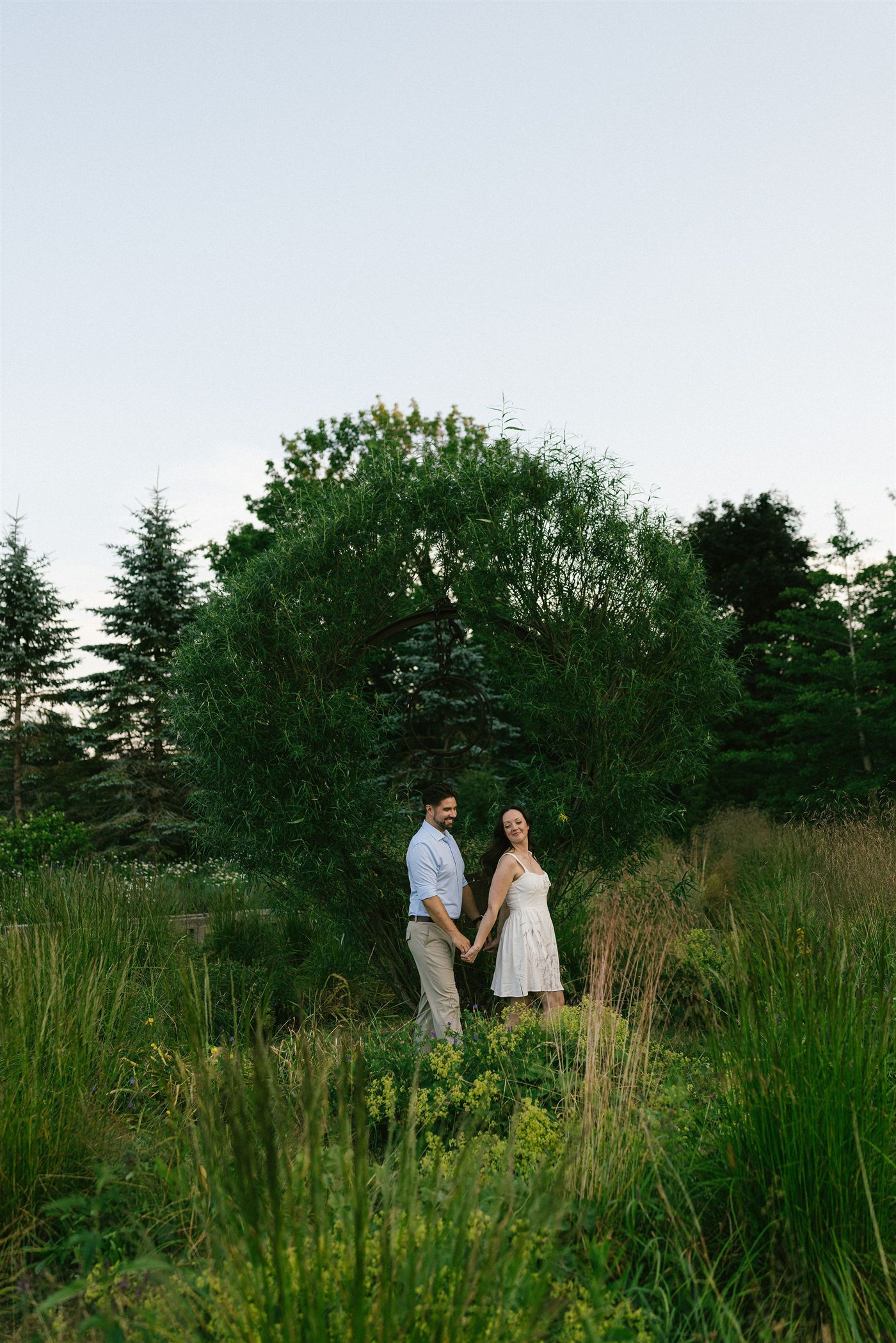 Danielle and Brenden holding hands beneath a willow arch
